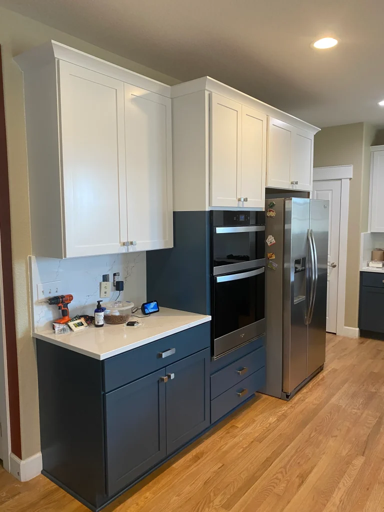 Refaced kitchen cabinets in Denver featuring white uppers, navy island, and updated hardware
